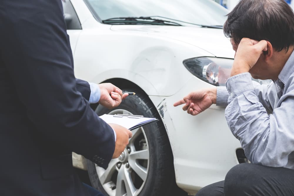 Agent filling insurance form near damaged car, illustrating the concept of traffic accidents and insurance claims.