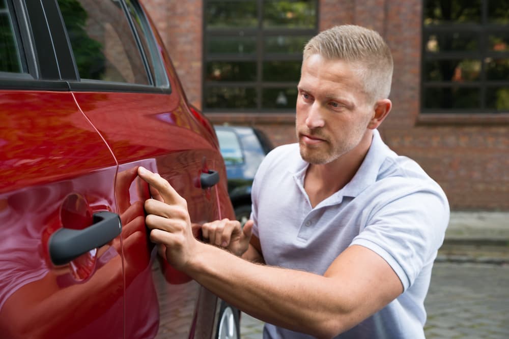 A close-up of a young man inspecting his red car for scratches or damages.