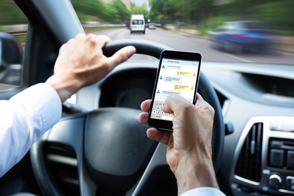 Close-up of a man's hand texting on a mobile phone while driving a car.






