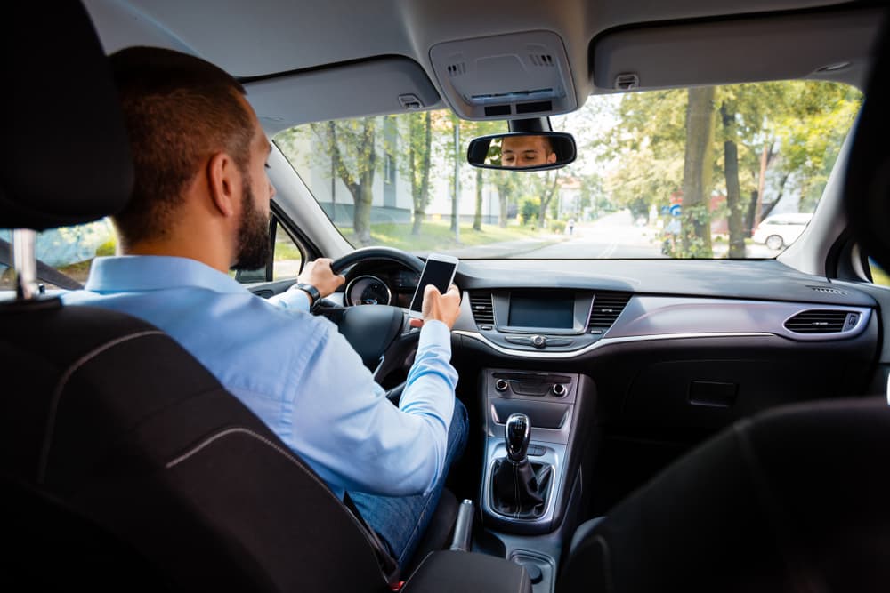 Young businessman texting on mobile phone while driving, viewed from behind.