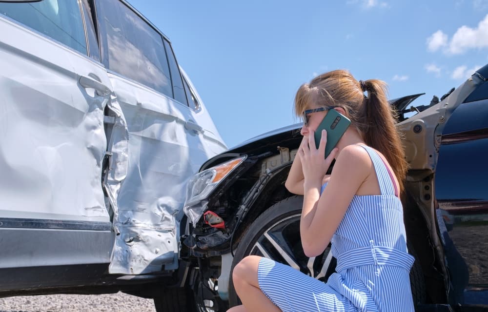 Female driver speaking on sellphone on street side calling for emergency service after car accident.